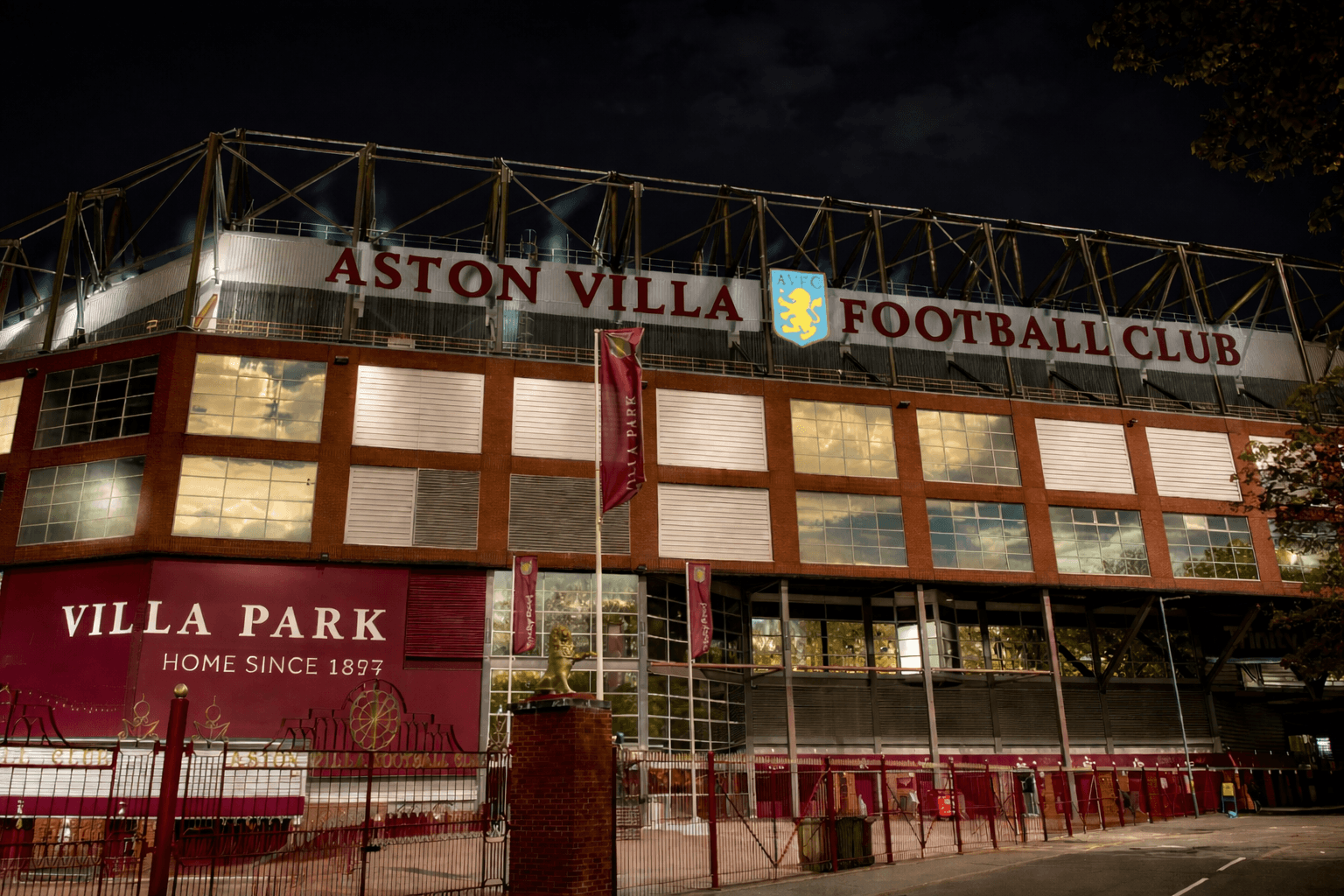 Villa Park stadium exterior at night, home of Aston Villa Football Club, red brick facade and stadium sign above the entrance