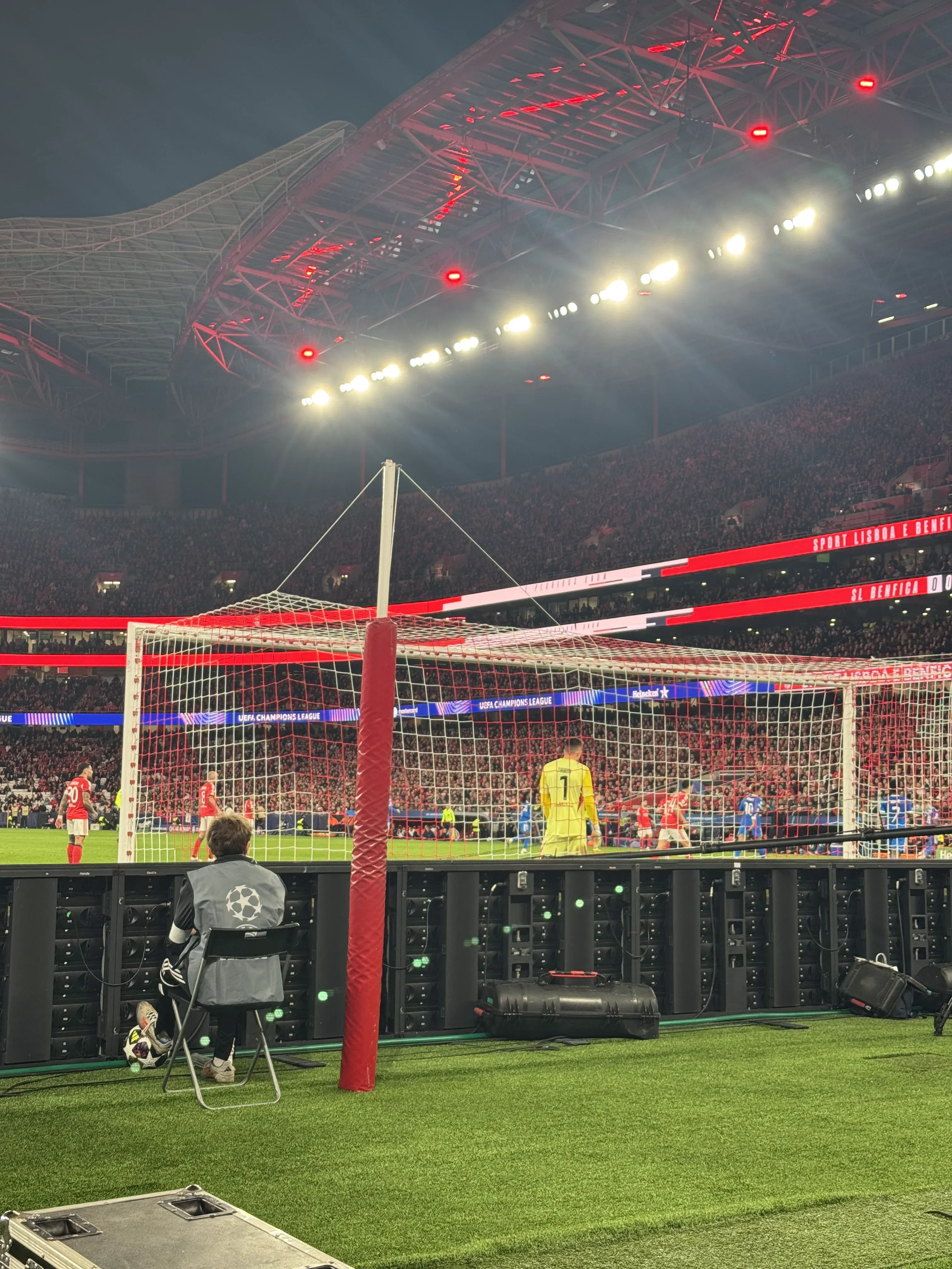 Pitchside view behind the goal during a Benfica Champions League night match at Estádio da Luz, with the goalkeeper, LED boards, and a packed stadium in the background