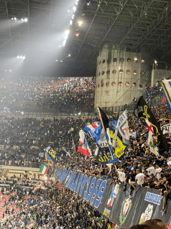 Inter Milan ultras in the Curva Nord at San Siro stadium waving flags and banners during an atmospheric night match in Milan