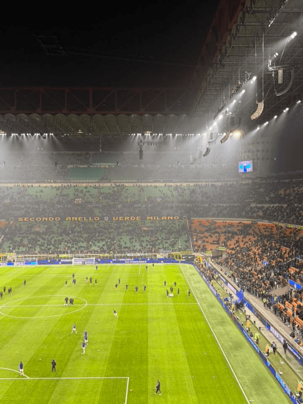 San Siro stadium at night during an Inter Milan match, with players warming up on the pitch and fans filling the iconic stands of the Giuseppe Meazza stadium in Milan